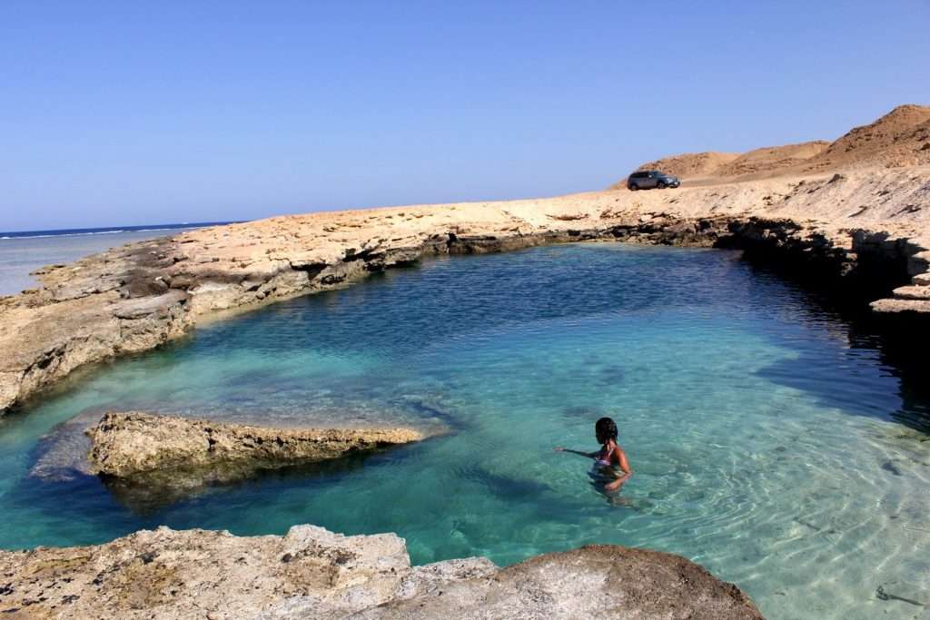 a woman is swimming in a shallow pool in the desert.